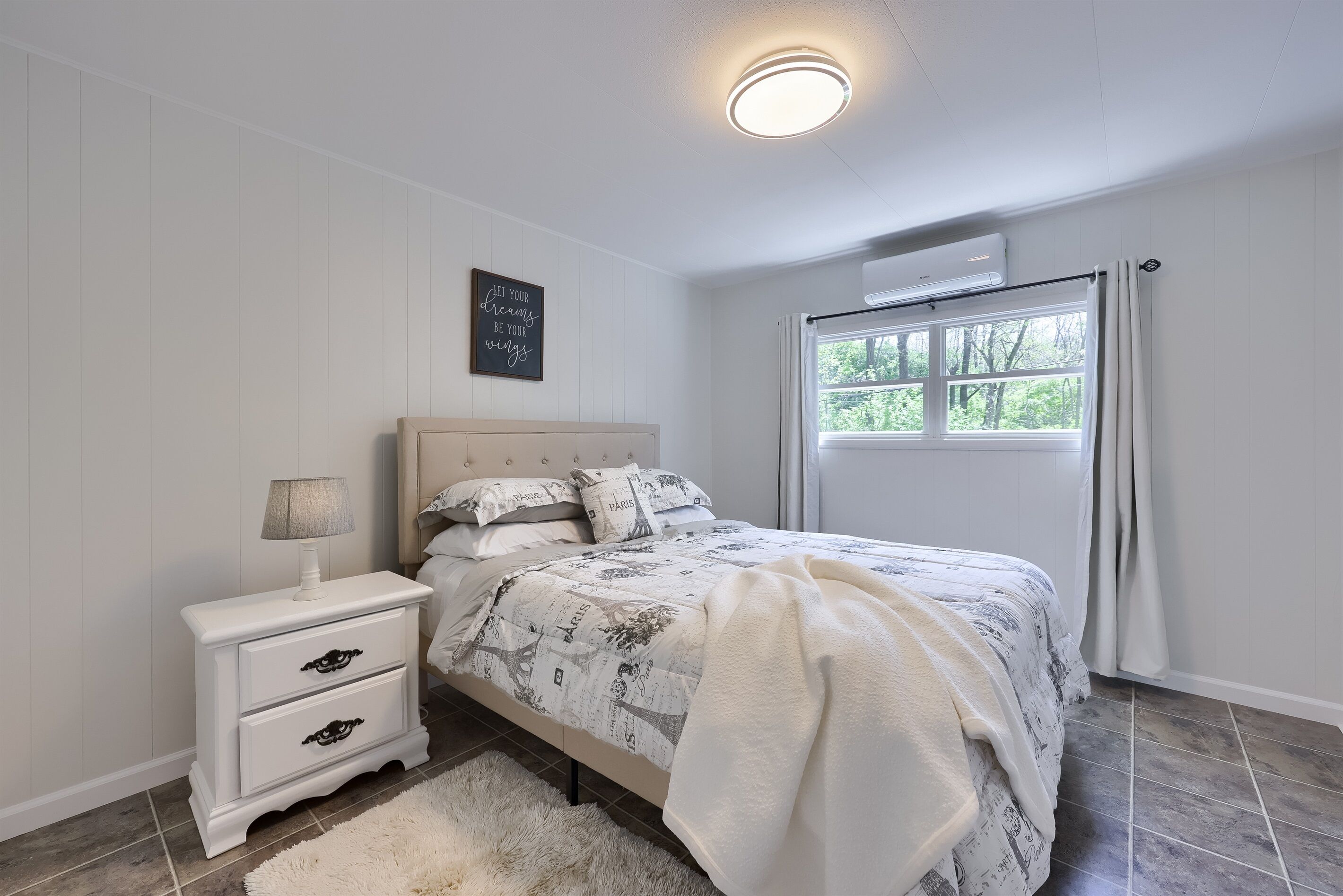 A bedroom with a bed, nightstand, and a window with curtains.
