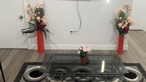 Un salon moderne avec un téléviseur à écran plat fixé au mur, deux vases rouges de chaque côté, une table basse en verre et des coussins gris et orange.