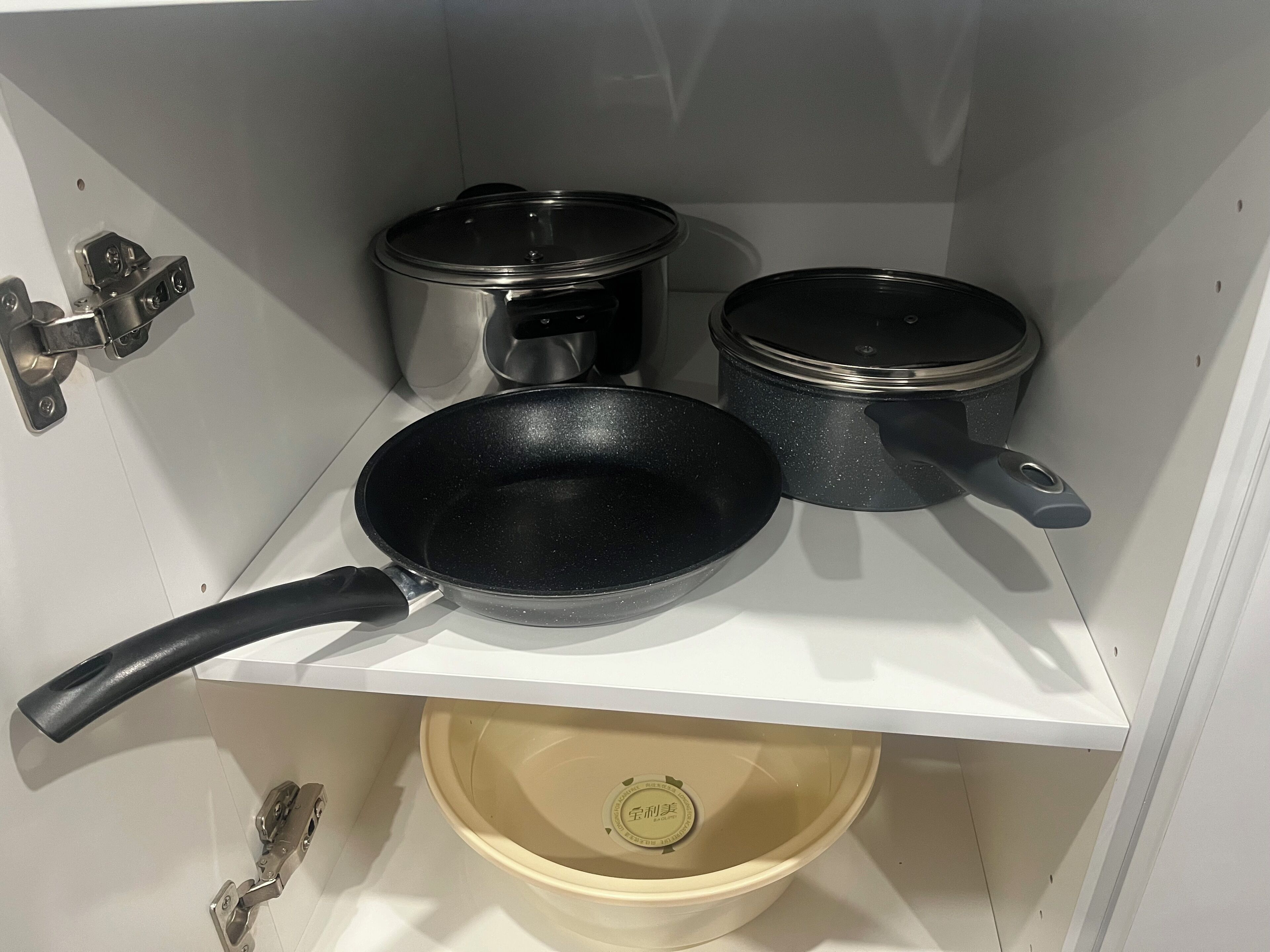 Eine Küche mit weißer Arbeitsplatte, drei Töpfen, einer Pfanne und einer beigen Schüssel.