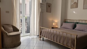 A bedroom with a bed, a chair, a nightstand, and a balcony.