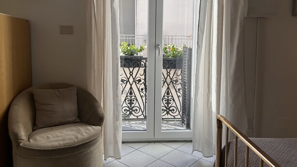 A room with a sliding glass door leading to a balcony with a wrought iron gate and potted plants.