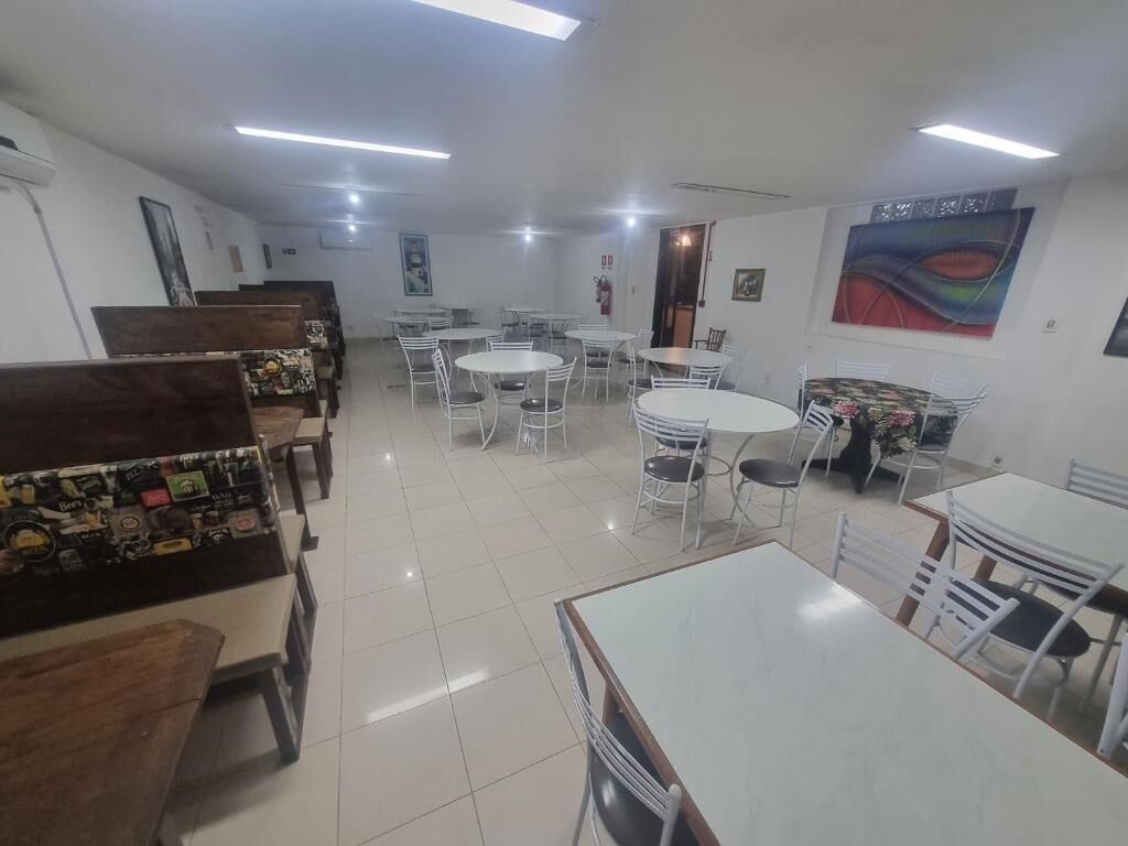 Uma área de refeições com várias mesas e cadeiras, um balcão com diversos itens e obras de arte nas paredes.