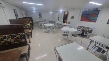 Uma área de refeições com várias mesas e cadeiras, um balcão com diversos itens e obras de arte nas paredes.