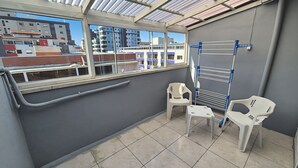 A balcony with a view of buildings, a drying rack, and two white plastic chairs. - Hotel Kolman (Capao da Canoa)