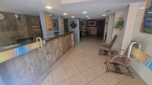A hotel reception area with a reception desk, a clock, and a seating area with wicker chairs. - Hotel Kolman (Capao da Canoa)