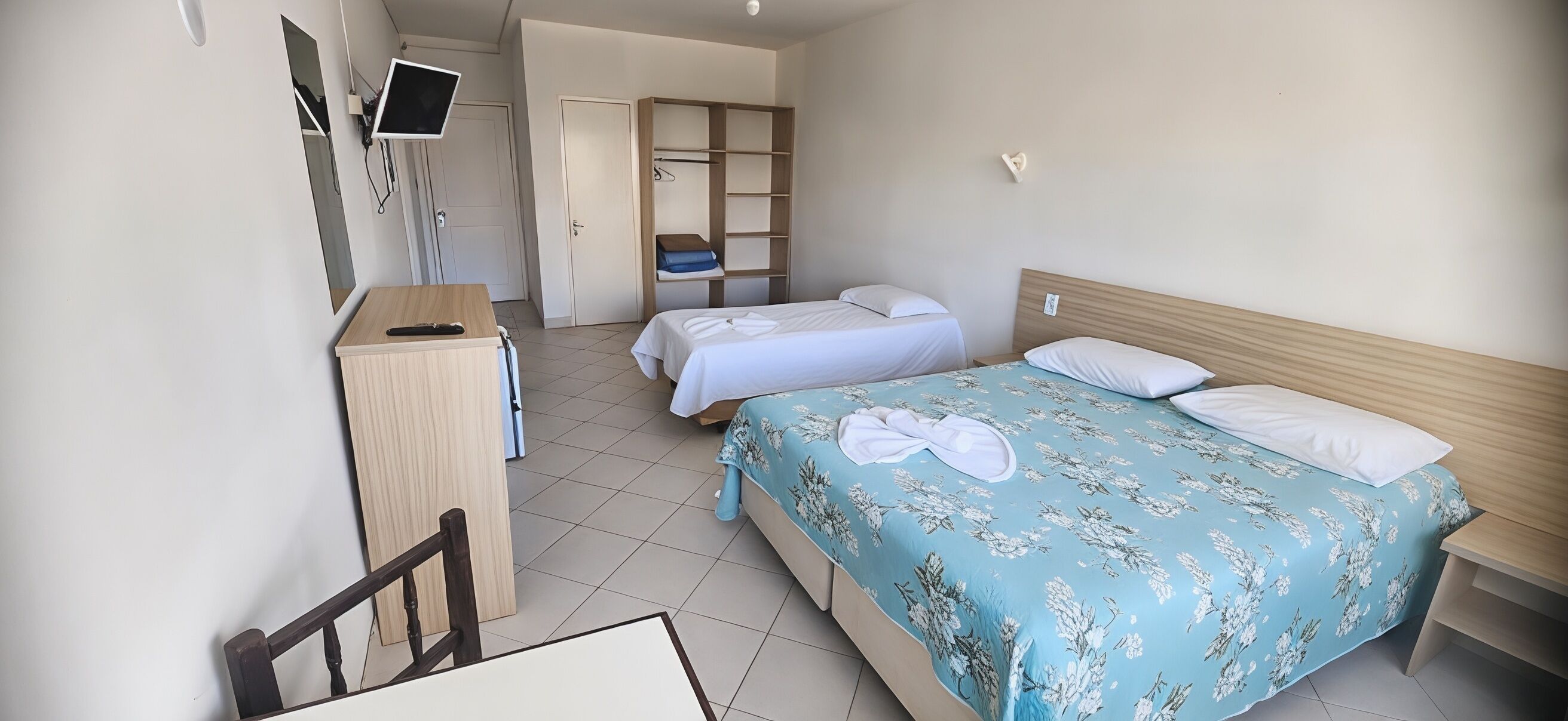 Una habitación de hotel con cama, escritorio, silla, televisor y armario.