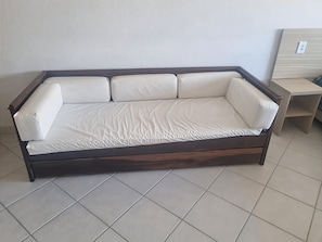A dark wood-framed sofa with white cushions in a room with tiled flooring. - Hotel Kolman (Capao da Canoa)