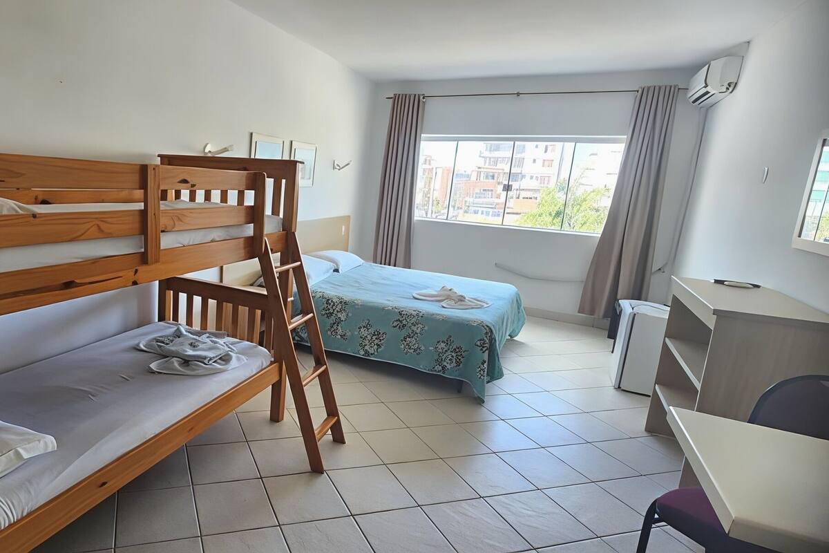 A room with bunk beds, a desk, a chair, a bed with a floral bedspread, and a window with curtains.