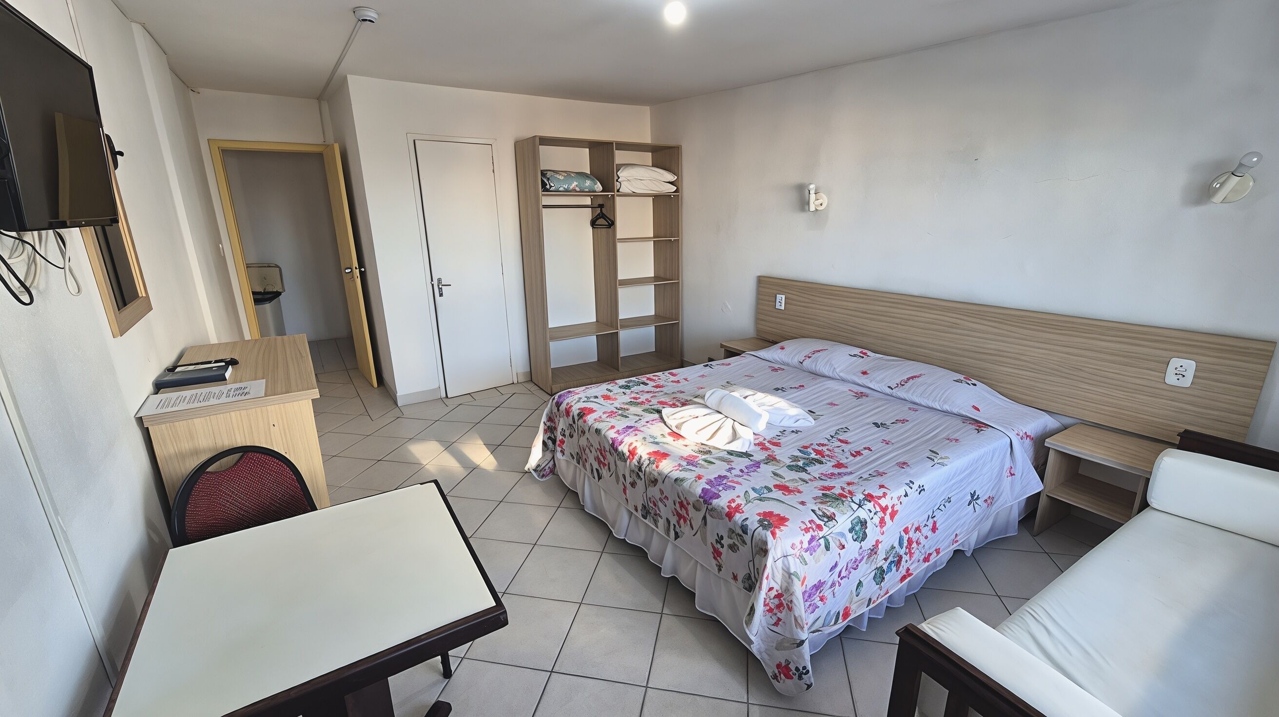 A hotel room with a bed, a desk, a chair, a wardrobe, and a bathroom door.