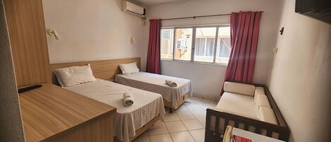 A hotel room with two beds, a wooden desk, a small sofa, and a window with curtains.
