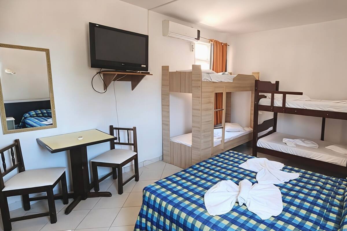 A room with bunk beds, a desk with a chair, a television, and a mirror.