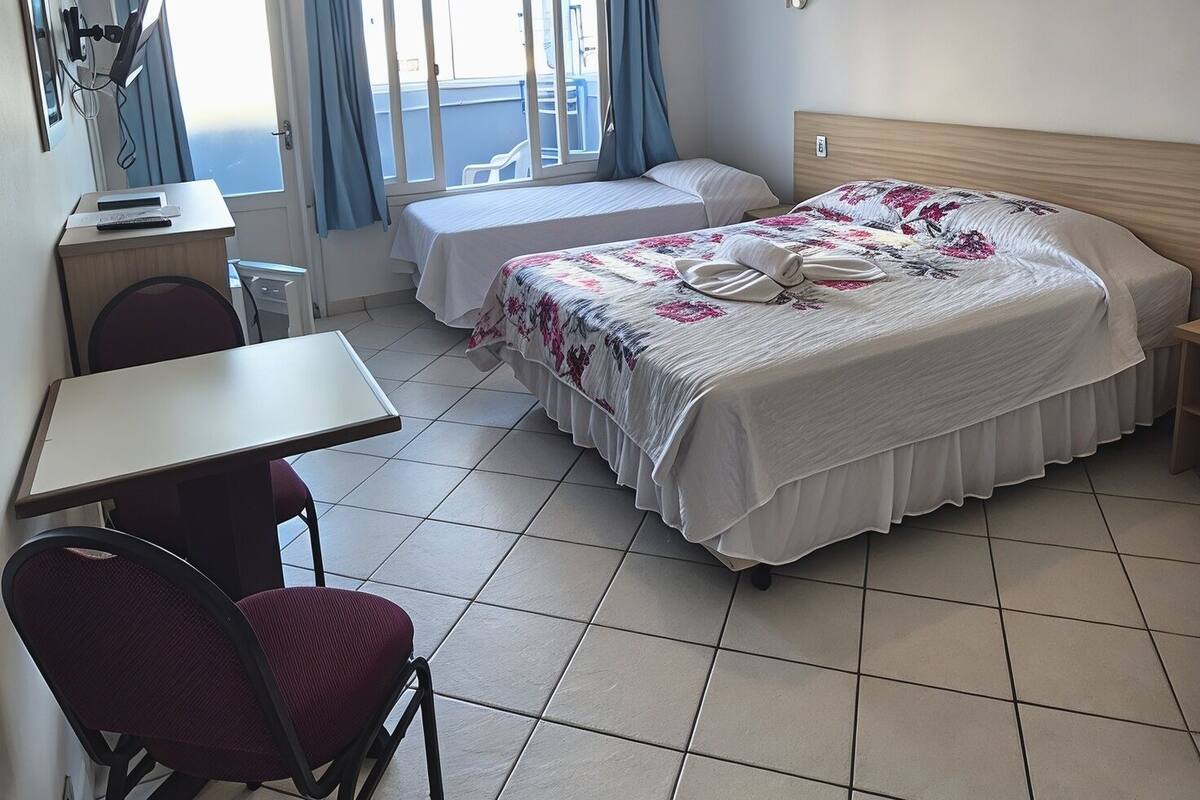 A hotel room with two beds, a desk, a chair, and a view of the sea.