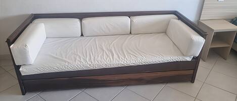 A dark wood-framed sofa with white cushions in a room with tiled flooring.