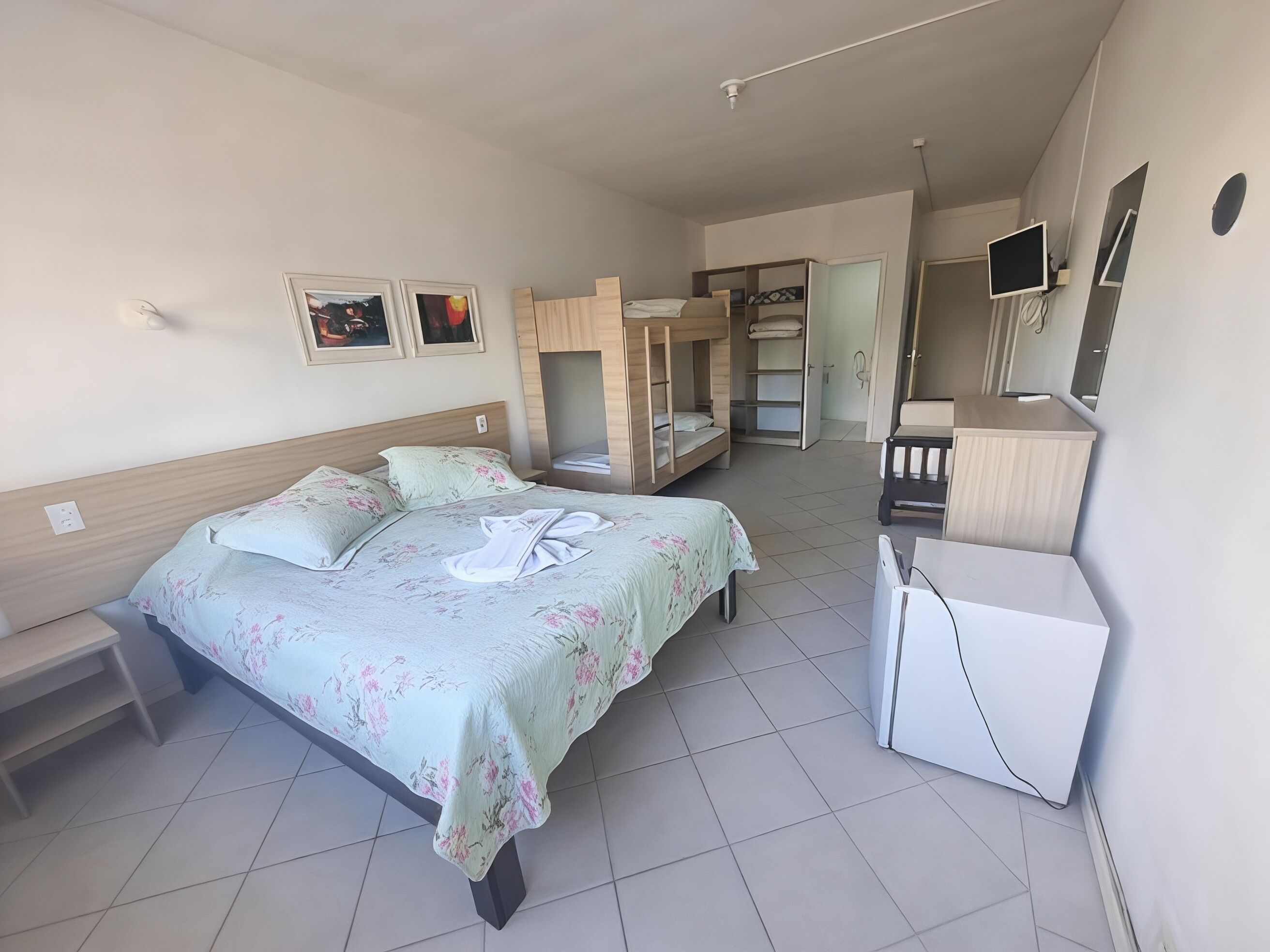 A bedroom with a bed, bunk beds, a desk, a chair, a wardrobe, and a TV.