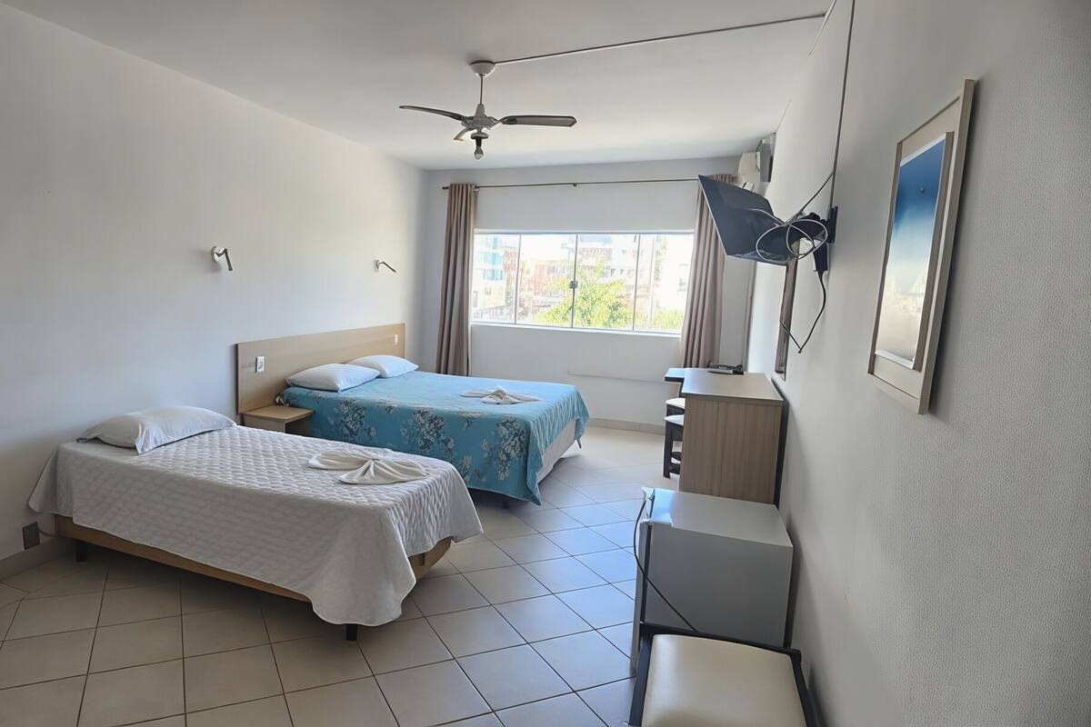 A hotel room with two beds, a ceiling fan, a desk, a chair, and a window with curtains.