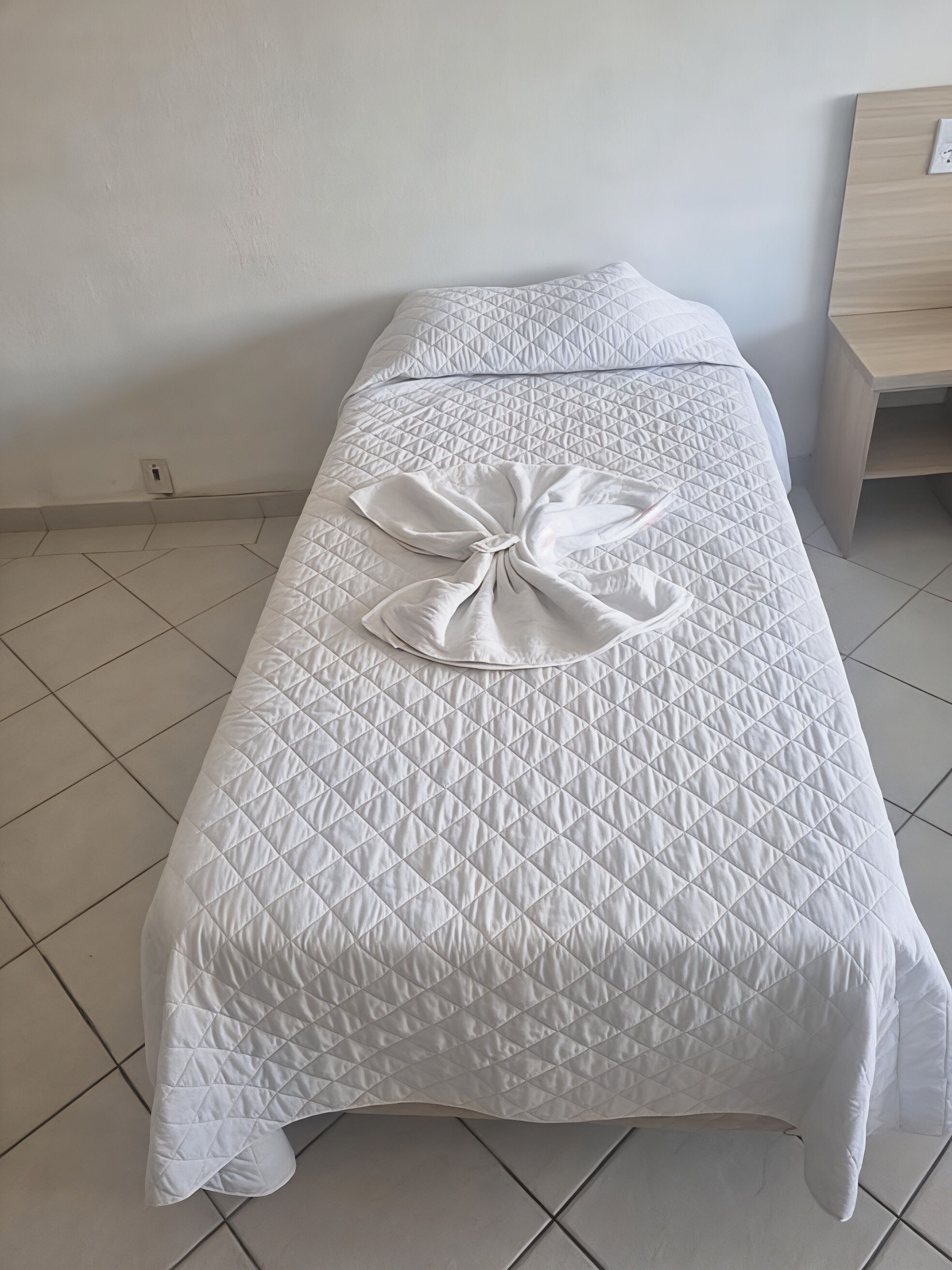 A neatly made bed with a quilted cover and a bow on the bedspread.