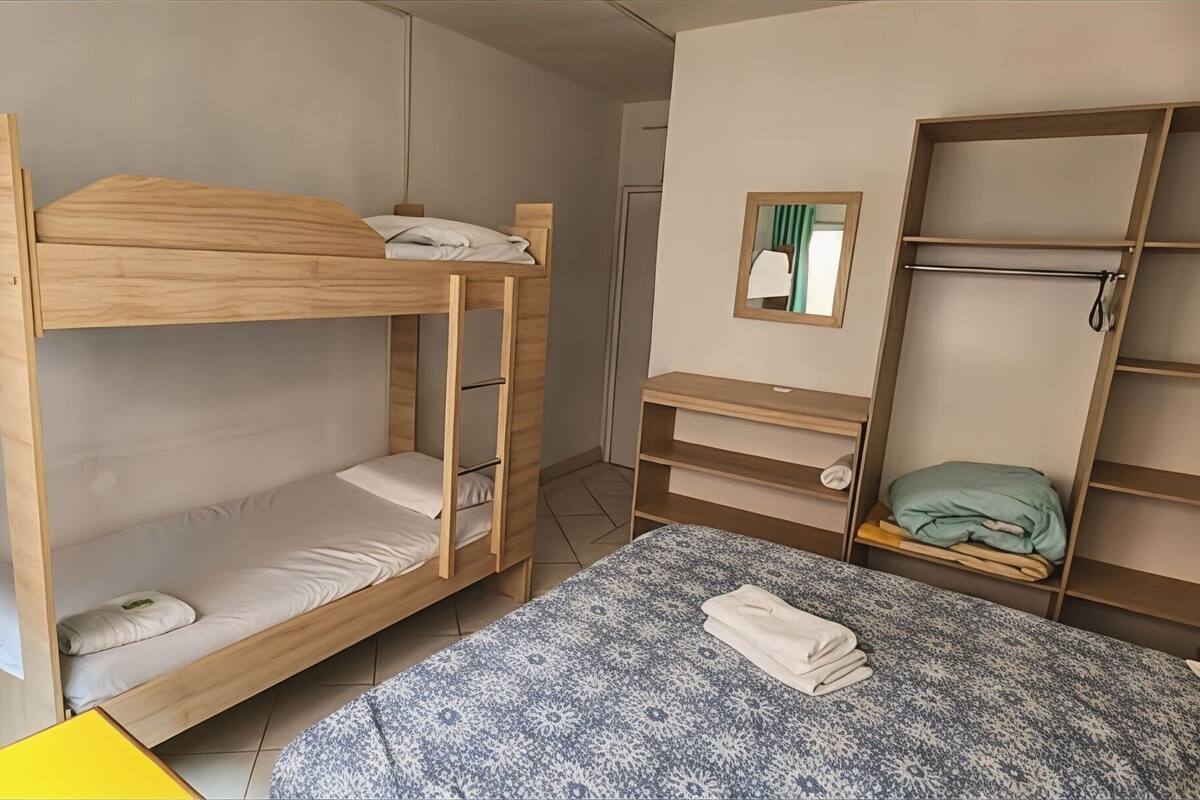A bunk bed with a TV on a shelf above, a desk with a mirror, and a wardrobe with shelves.