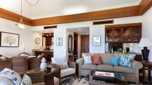 A spacious living room with wicker furniture, a sofa with colorful cushions, and a dining area with wooden cabinets. - Mauna Lani Resort  Terrace - G301 - BEST VIEWS - Updated - Owners Club Access (Kamuela)