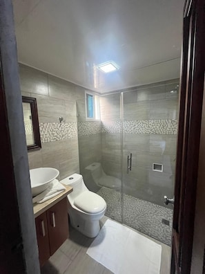 A modern bathroom with a glass-enclosed shower, a white toilet, and a vanity with a mirror.