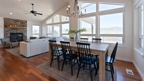 A spacious living room with a fireplace, a dining area with a wooden table and chairs, and large windows offering a view of the outdoors.