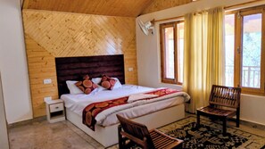 A bedroom with a wooden headboard, a bed with a patterned blanket, two wooden chairs, and a window with curtains.