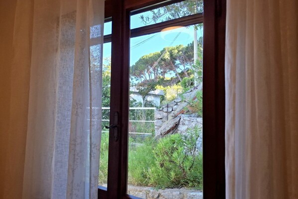 A window with a view of a stone wall and greenery outside.