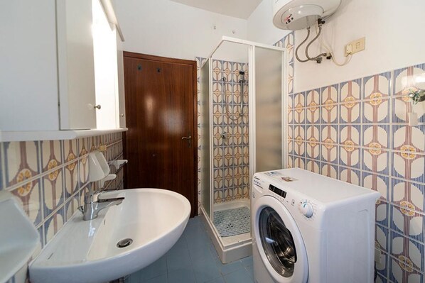 Une salle de bain avec un lavabo, un lave-linge, une douche et une porte.