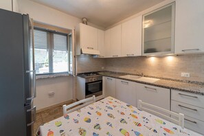 Una cucina compatta con mobili bianchi, un fornello a gas, un lavello e una finestra con persiane.