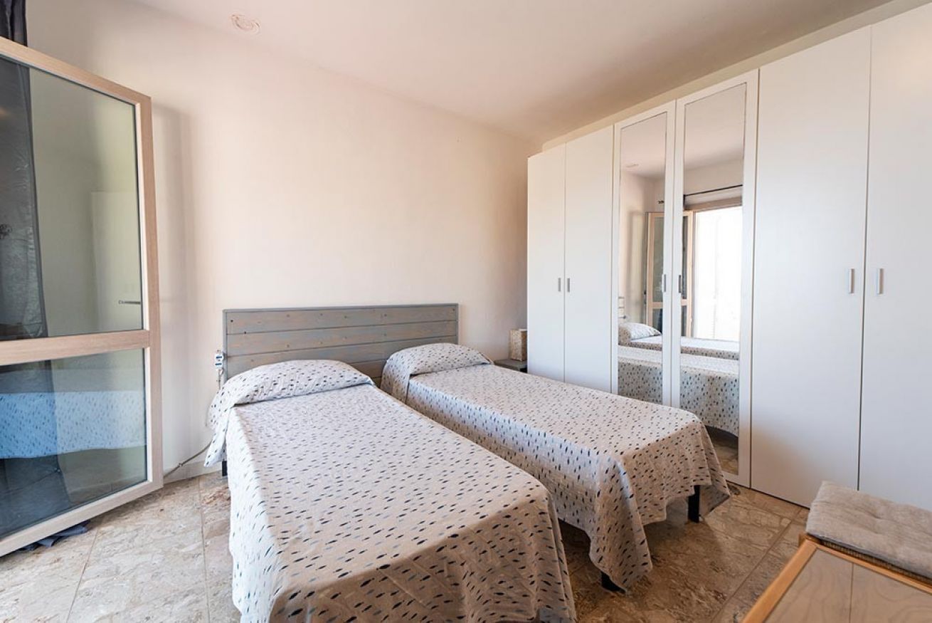 Quarto com duas camas, um guarda-roupa e uma porta de vidro deslizante.