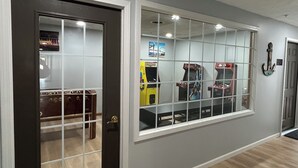 A hallway with a dark door, a window with arcade games, and a wall-mounted guitar.