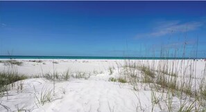 A beach with white sand and sparse grass in the foreground, leading to a calm blue ocean under a clear sky. - Sarasota Poolside Stylish Retreat w/Grill, Fishing (Sarasota)