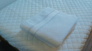 A neatly made bed with a quilted mattress and a folded white blanket. - Interfaith 21 (New York)