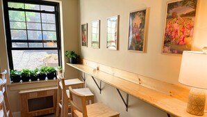 A room with a long wooden bench, a window with potted plants, and framed artwork on the wall. - Interfaith 21 (New York)