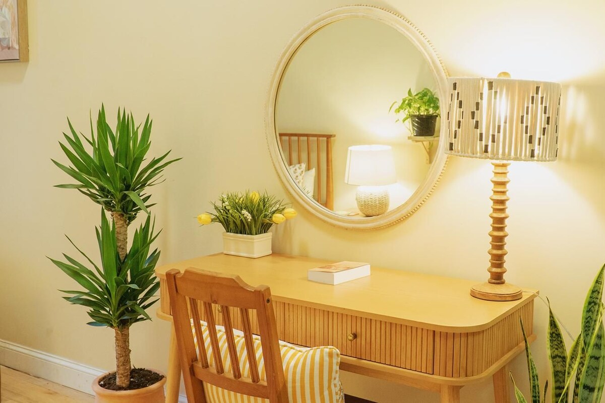 A wooden desk with a mirror, a lamp, and two potted plants.
