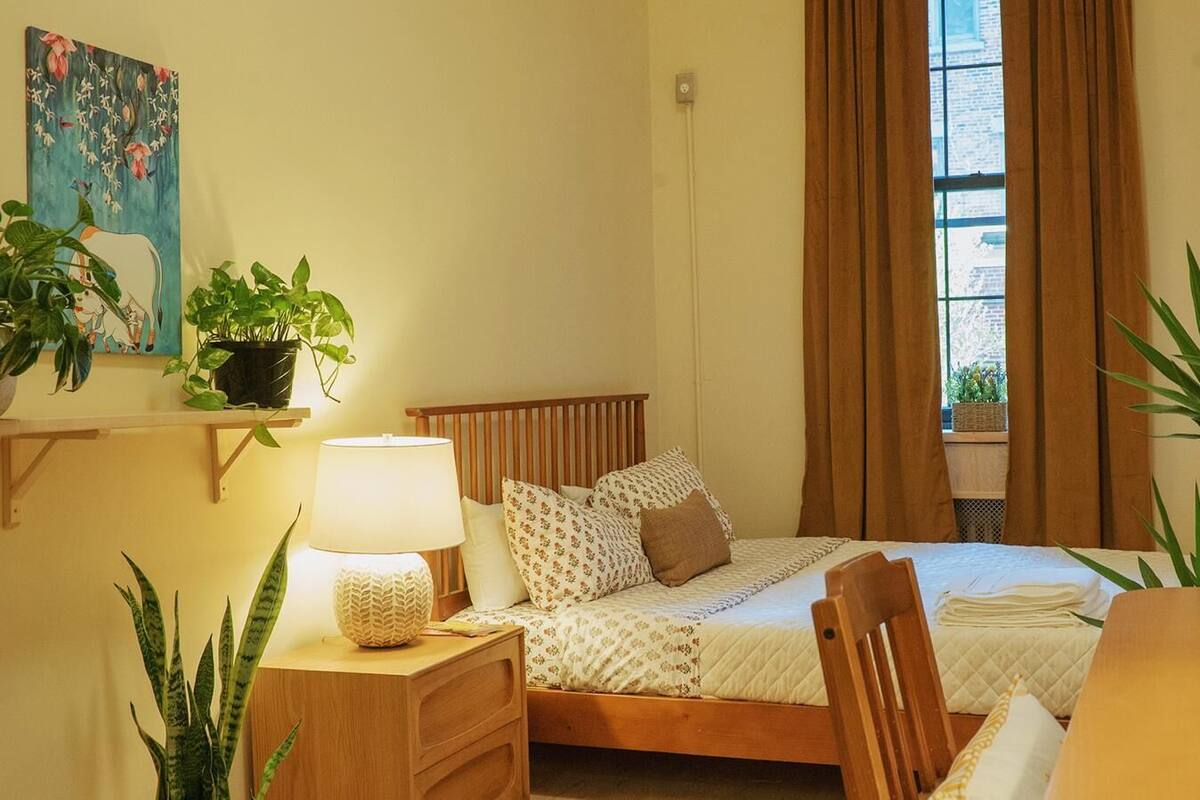 A neatly arranged bedroom with a bed, bedside tables, a lamp, and potted plants.
