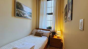 A small, cozy bedroom with a bed, a nightstand with a lamp, and a window with curtains.