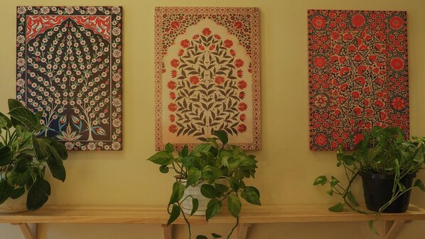 Three framed floral artworks on a wall, with potted plants in front. - Interfaith 21 (New York)
