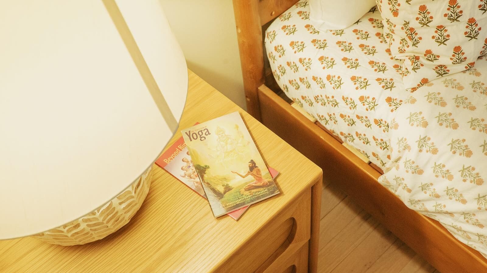 A wooden bedside table with a lamp and a yoga book.