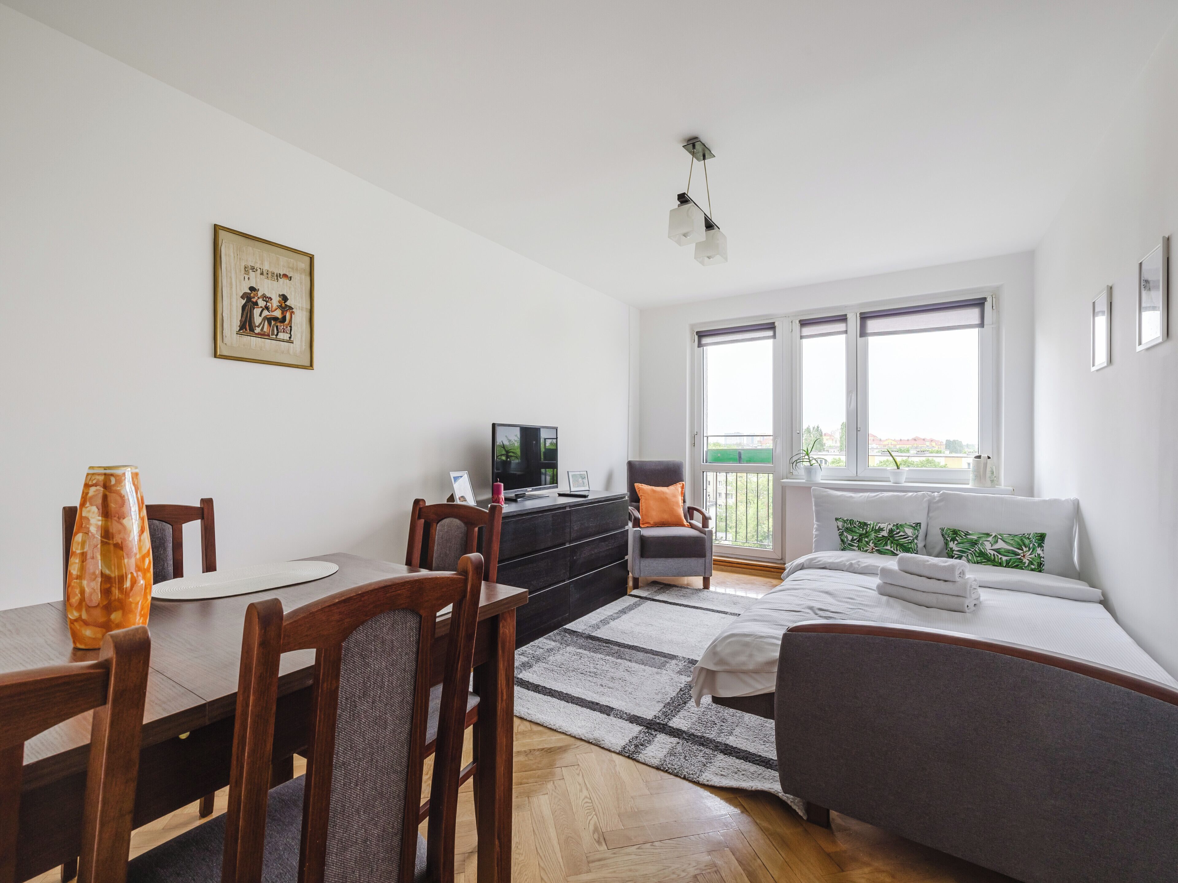 A modern, well-lit room with a dining area, a sofa, a bed, and a TV.