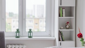 A room with a white radiator, a window with two green lanterns, a bookshelf with books and a vase, and a red rose.