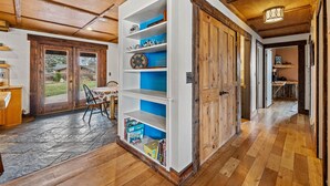 Un intérieur en bois agrémenté d’une bibliothèque intégrée, un coin repas avec une table et des chaises, et un couloir menant à une autre pièce.