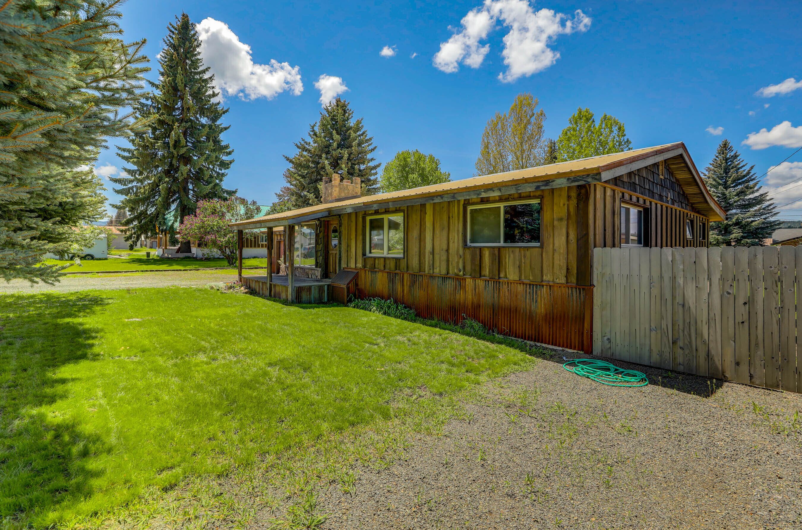 A rustic cabin with a wooden exterior, a porch, and a fenced yard.