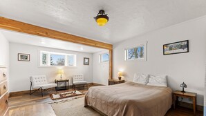 Une chambre avec un grand lit, des poutres en bois, un tapis, un bureau et une chaise.