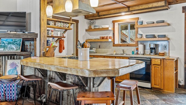 Une cuisine dotée d’un grand îlot central, de tabourets de bar, d’étagères en bois et d’un téléviseur.