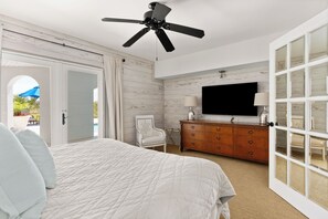 A bedroom with a bed, a ceiling fan, a TV, a dresser, and a chair. - Enchanted Hideaway: Extraordinary Oceanfront Escape | Ocean Views | Private Pool (Saint Simons Island)