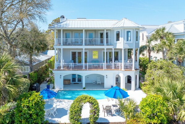 A two-story house with a pool, surrounded by lush greenery and palm trees. - Enchanted Hideaway: Extraordinary Oceanfront Escape | Ocean Views | Private Pool (Saint Simons Island)