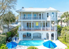 A two-story house with a balcony, a swimming pool, and a covered patio area. - Enchanted Hideaway: Extraordinary Oceanfront Escape | Ocean Views | Private Pool (Saint Simons Island)