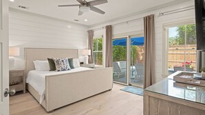 A bedroom with a bed, a ceiling fan, a glass coffee table, and a view of the outdoors. - Enchanted Getaway: Coastal Escape | Private Pool | Easy Walk to Beach + Village (Saint Simons Island)