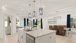 A modern kitchen with a central island, stainless steel appliances, and hanging pendant lights. - Enchanted Getaway: Coastal Escape | Private Pool | Easy Walk to Beach + Village (Saint Simons Island)