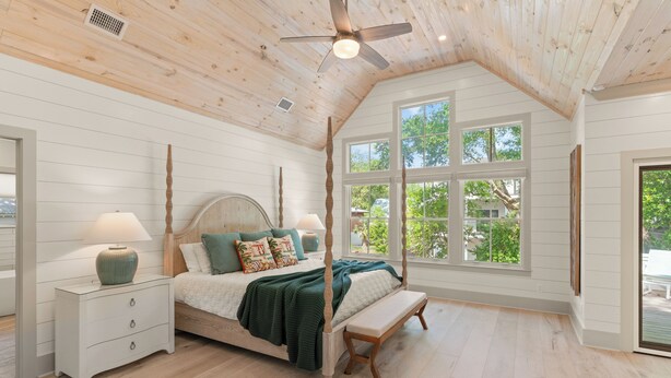 A bedroom with a four-poster bed, a wooden bench, a nightstand, and a large window with a view of trees. - Enchanted Getaway: Coastal Escape | Private Pool | Easy Walk to Beach + Village (Saint Simons Island)